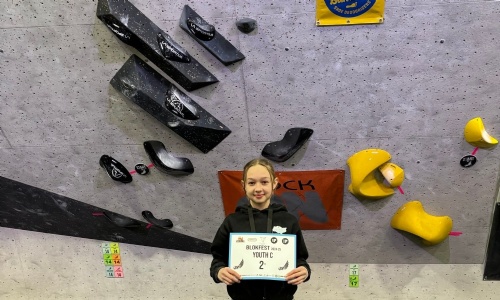 Picture of a student standing in front of a climbing wall holding a certificate